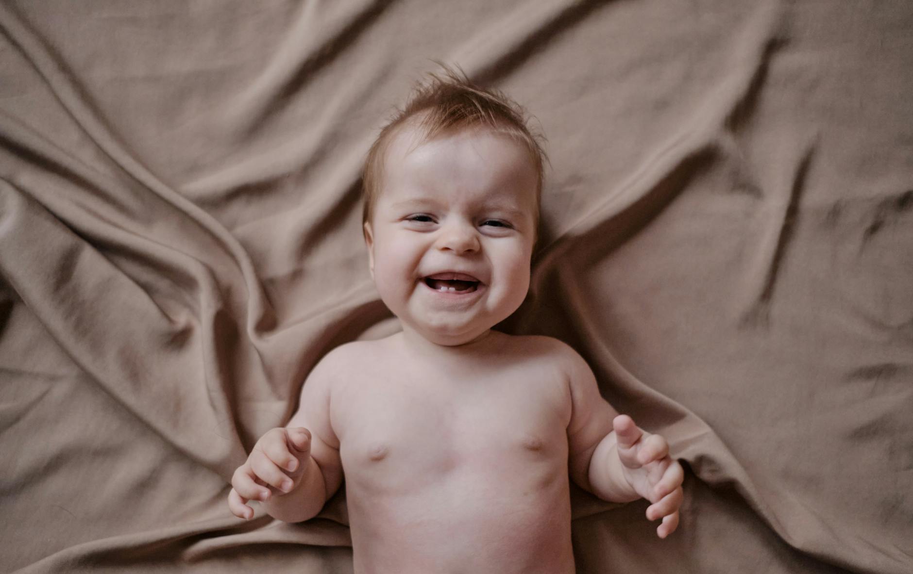 Baby — A happy baby laughing while lying on a soft, neutral-colored fabric, capturing pure joy.