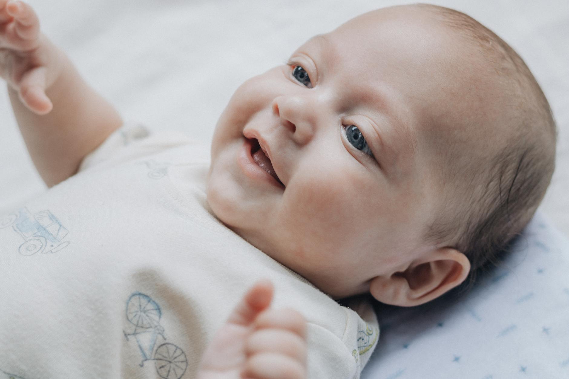 Baby — Adorable baby smiling and lying on a soft blanket, expressing happiness and warmth.
