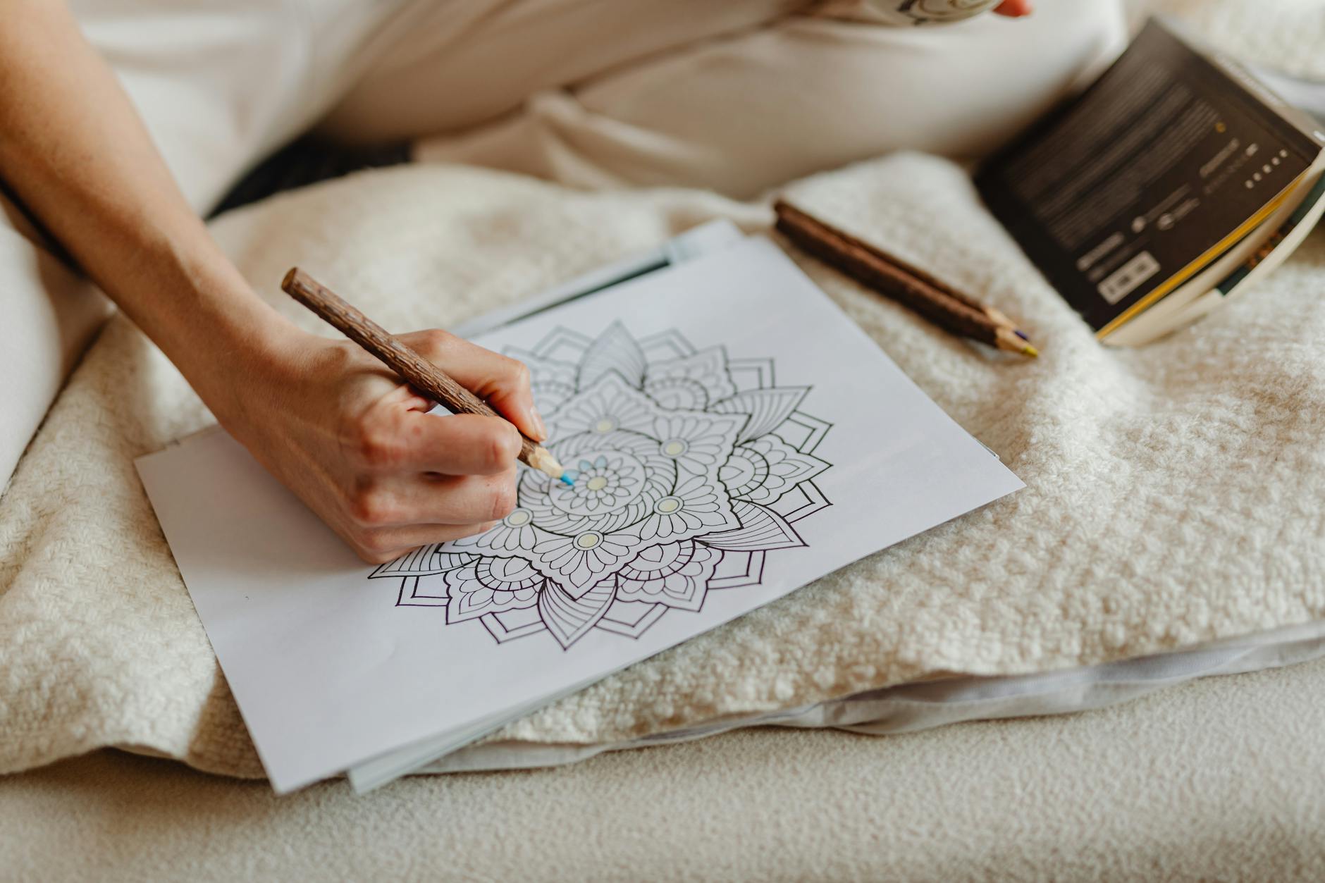 Coloring Page — Person uses a brown pencil to color a mandala drawing on paper, creating art indoors.