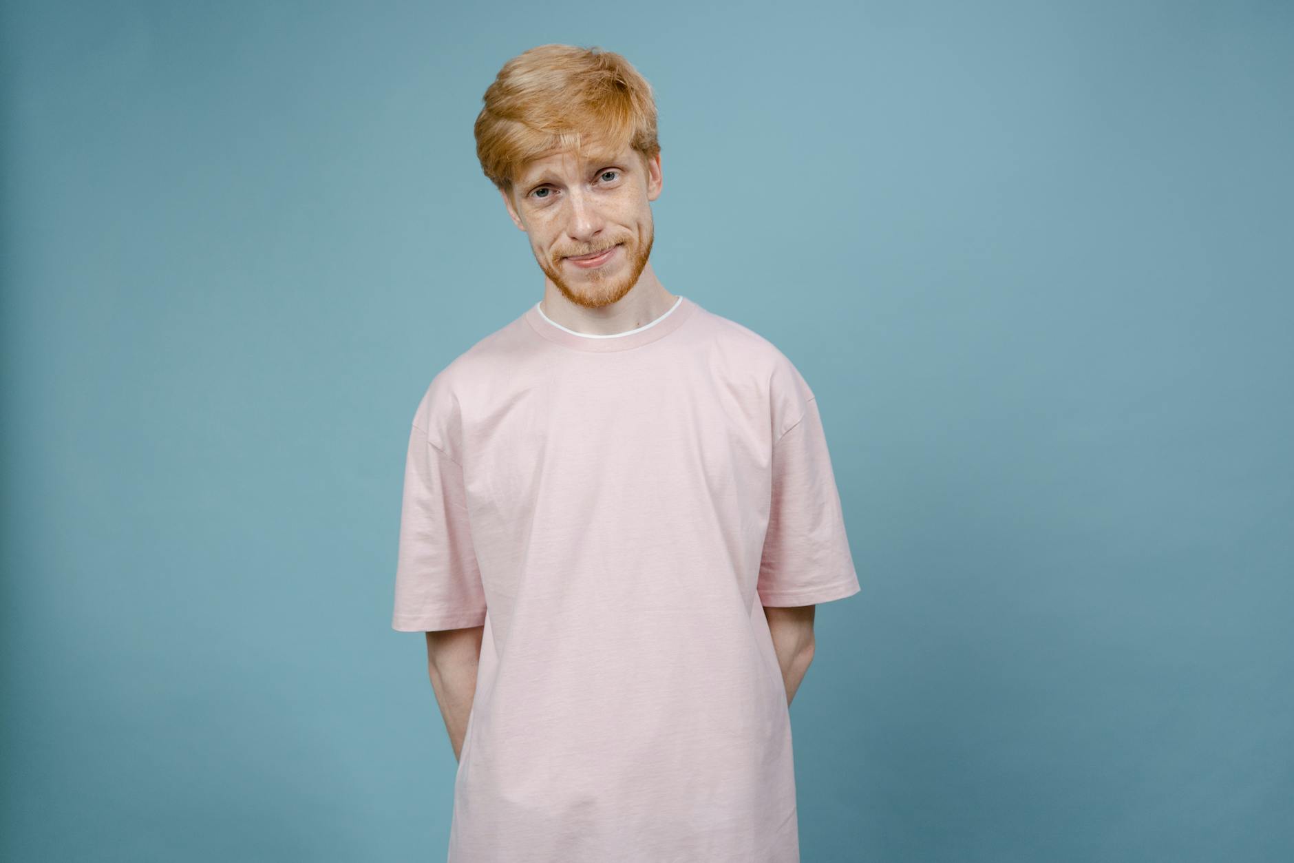 Face Swap — Portrait of a smiling young man in a pastel pink t-shirt against a plain blue background.