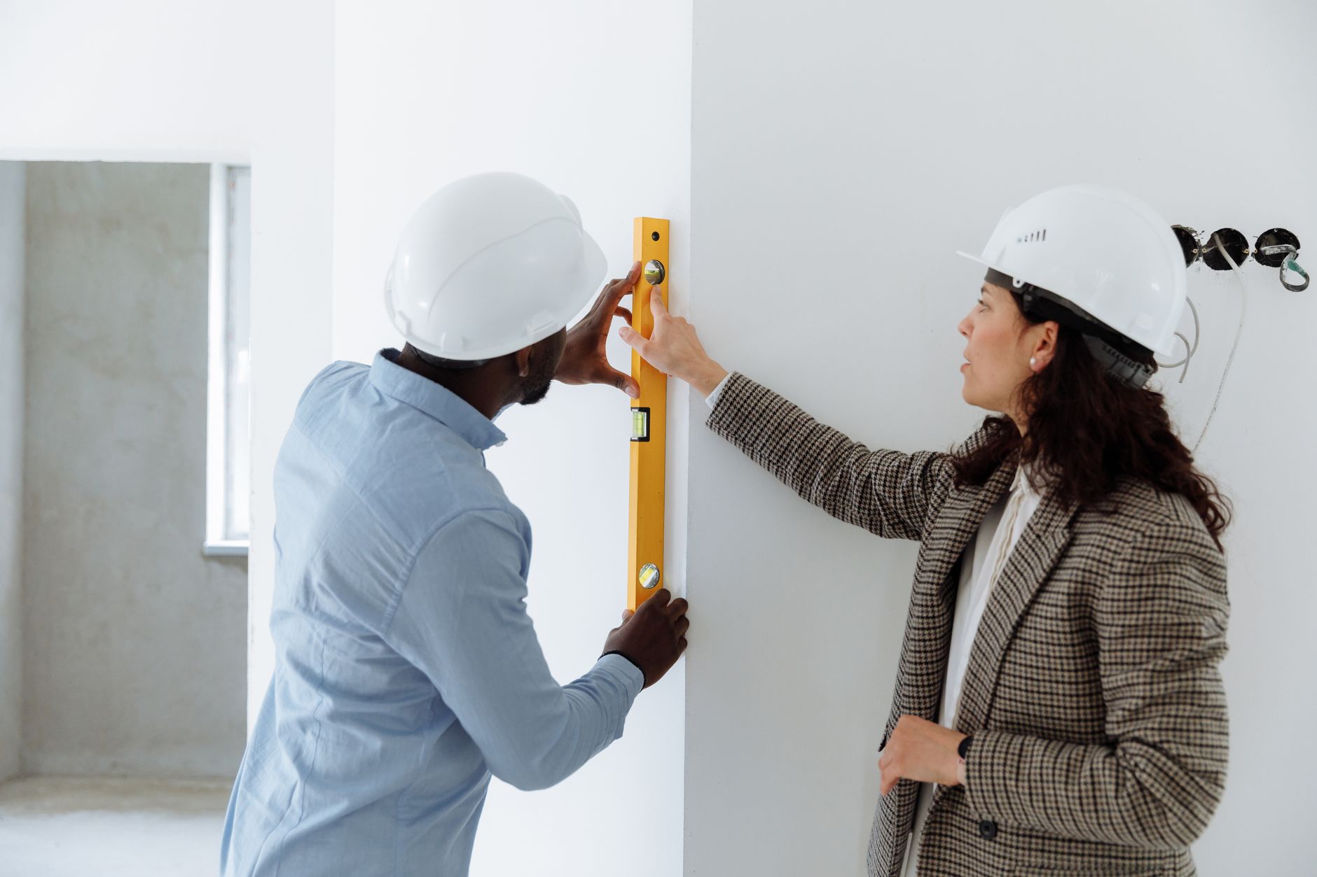 For Construction, Construction Assistant, For Building, For Contractors — Two contractors using a level bar to check wall alignment inside a