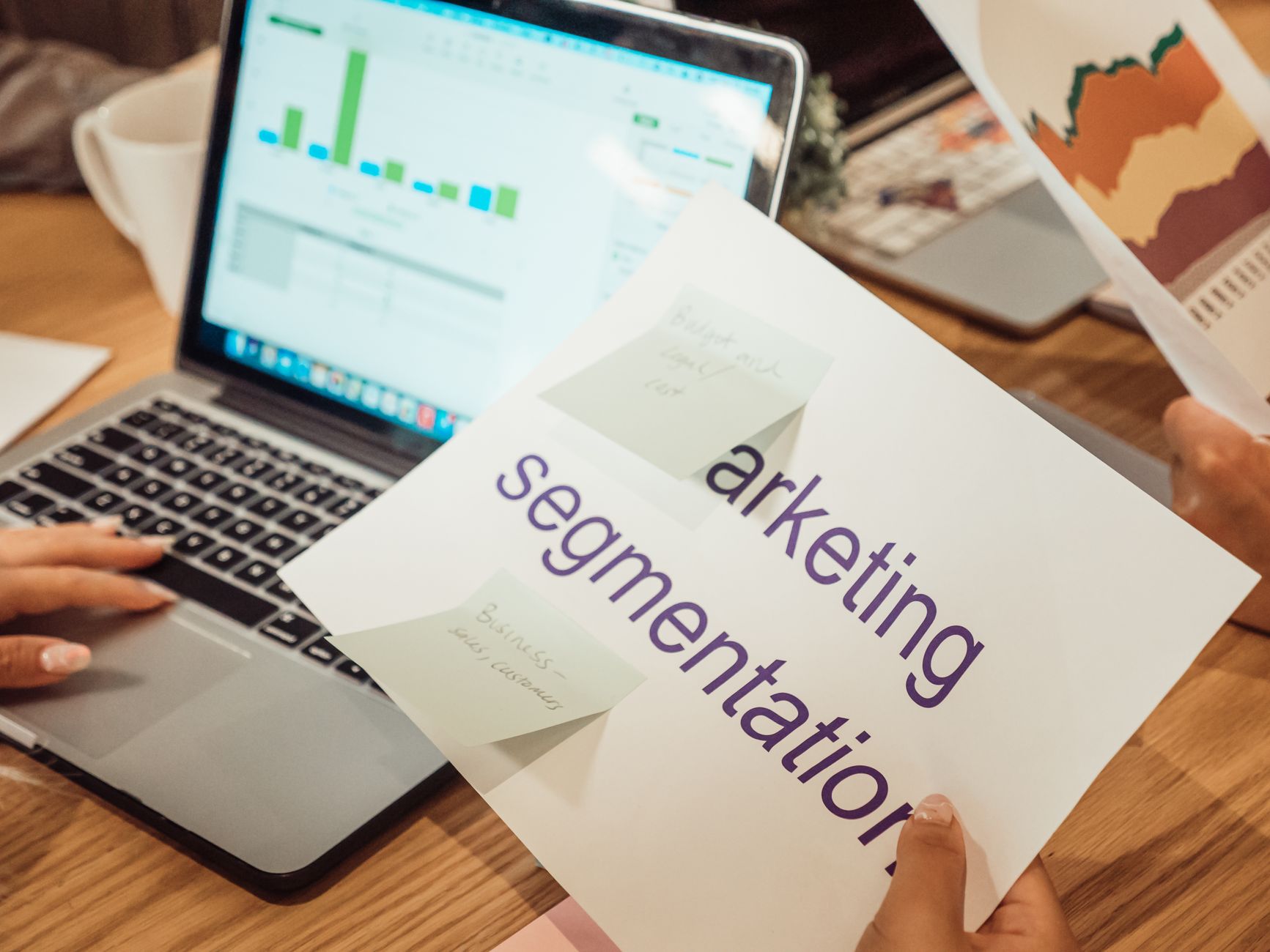For Marketing, Marketing Assistant, For Marketers — A modern workspace showing hands analyzing marketing data on a laptop and paper document