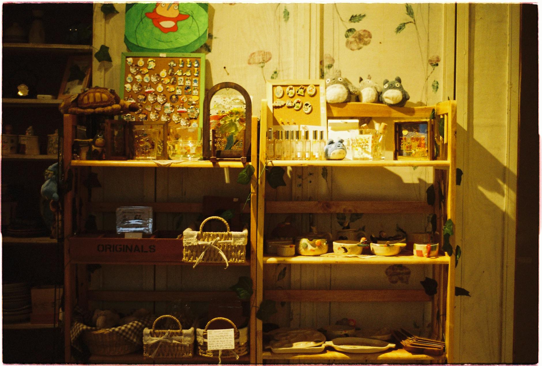 Ghibli Art — A warm, inviting display of Totoro collectibles on wooden shelves in a cozy shop setting.