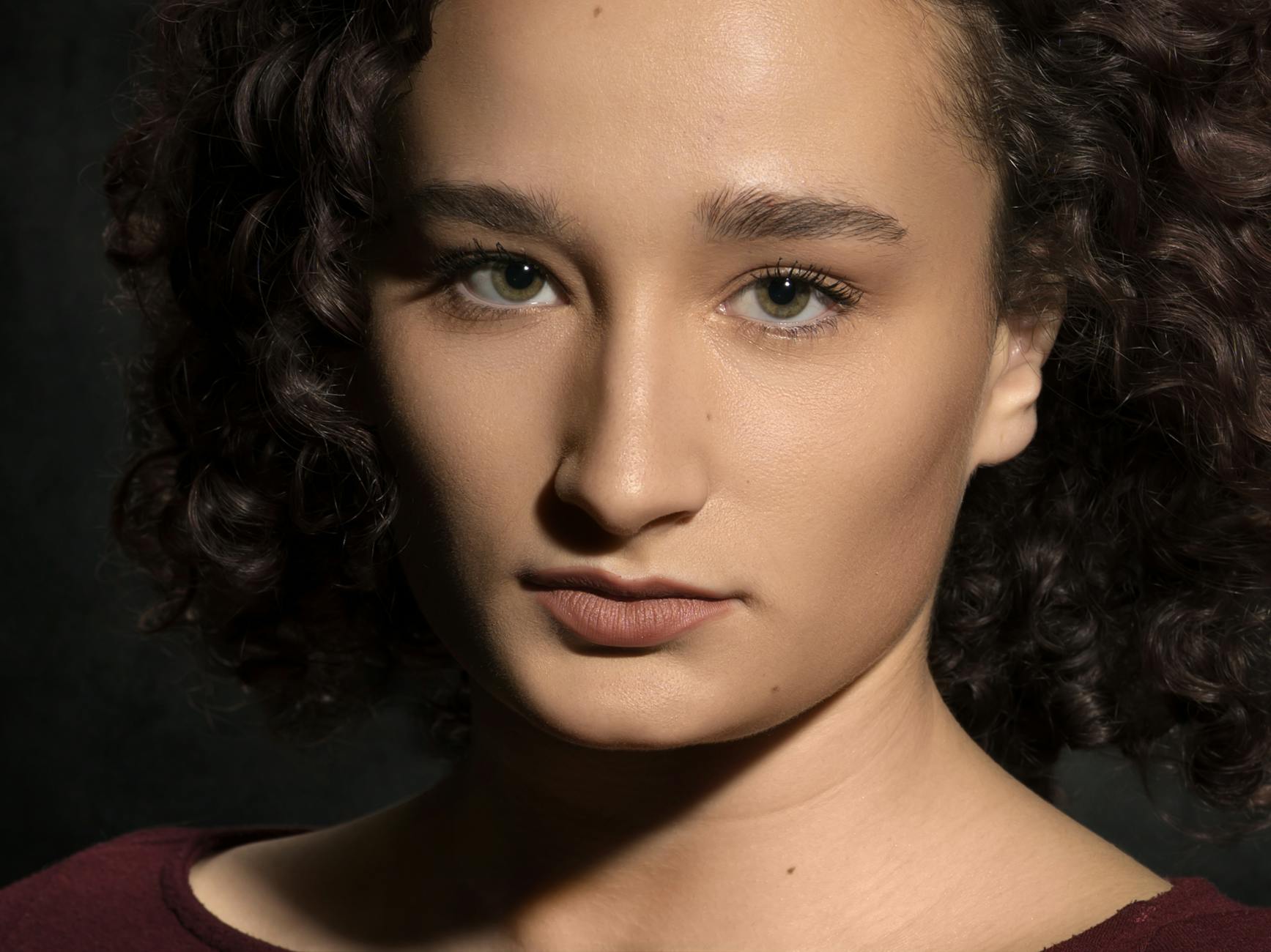 Headshot — A striking close-up portrait capturing a woman with curly hair against a dark background.