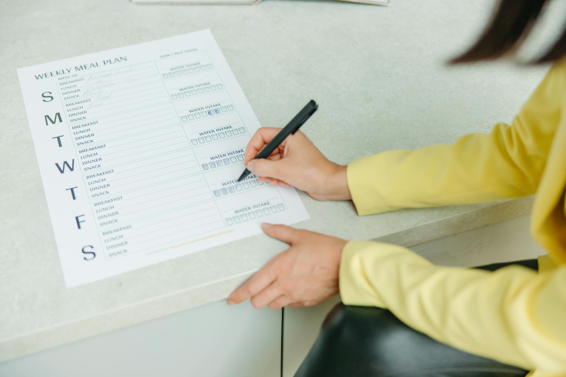 Meal Planner, Meal Plan, Diet Plan — Woman writing on a weekly meal plan checklist indoors, focusing on diet organization.