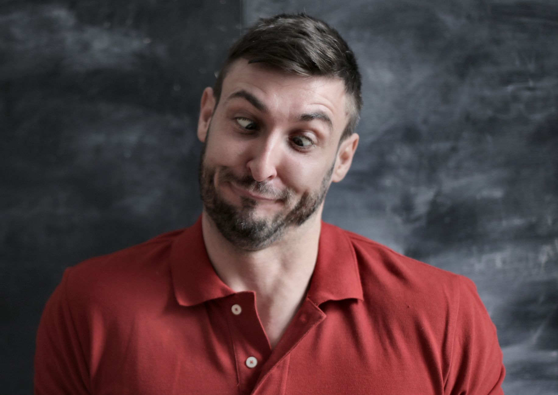 Amusing portrait of a man making a wacky facial expression in a red polo shirt.