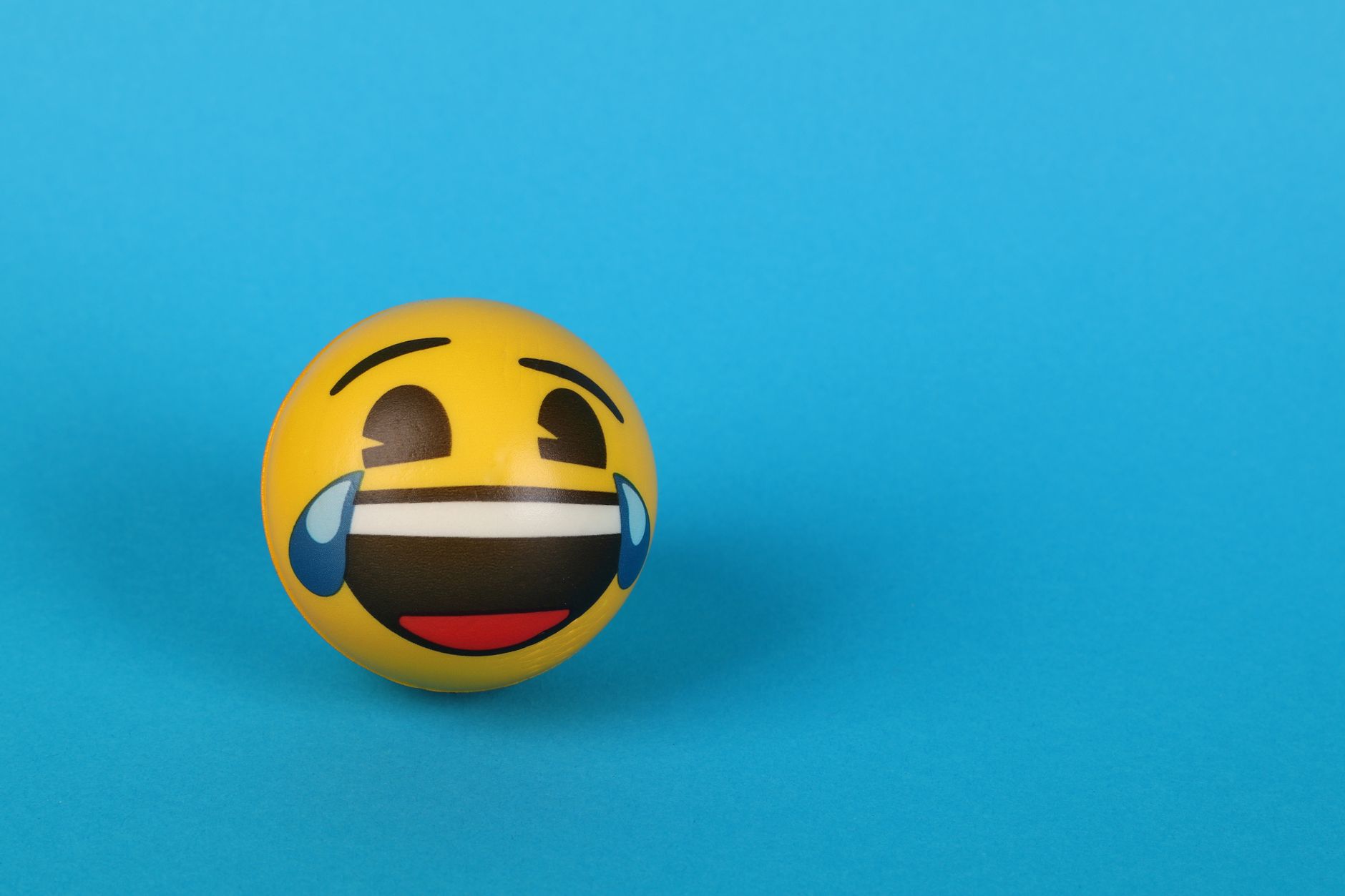 Vibrant yellow emoji ball with a laughing expression against a blue background.