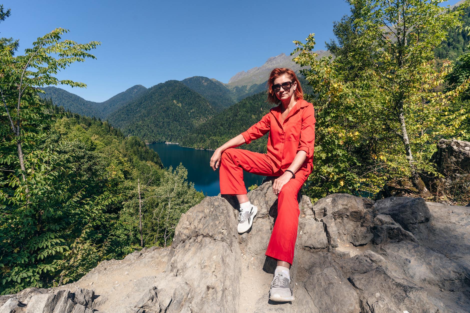 Outfit — Woman in red outfit posing on a rock with a scenic mountain lake view at Гагры.