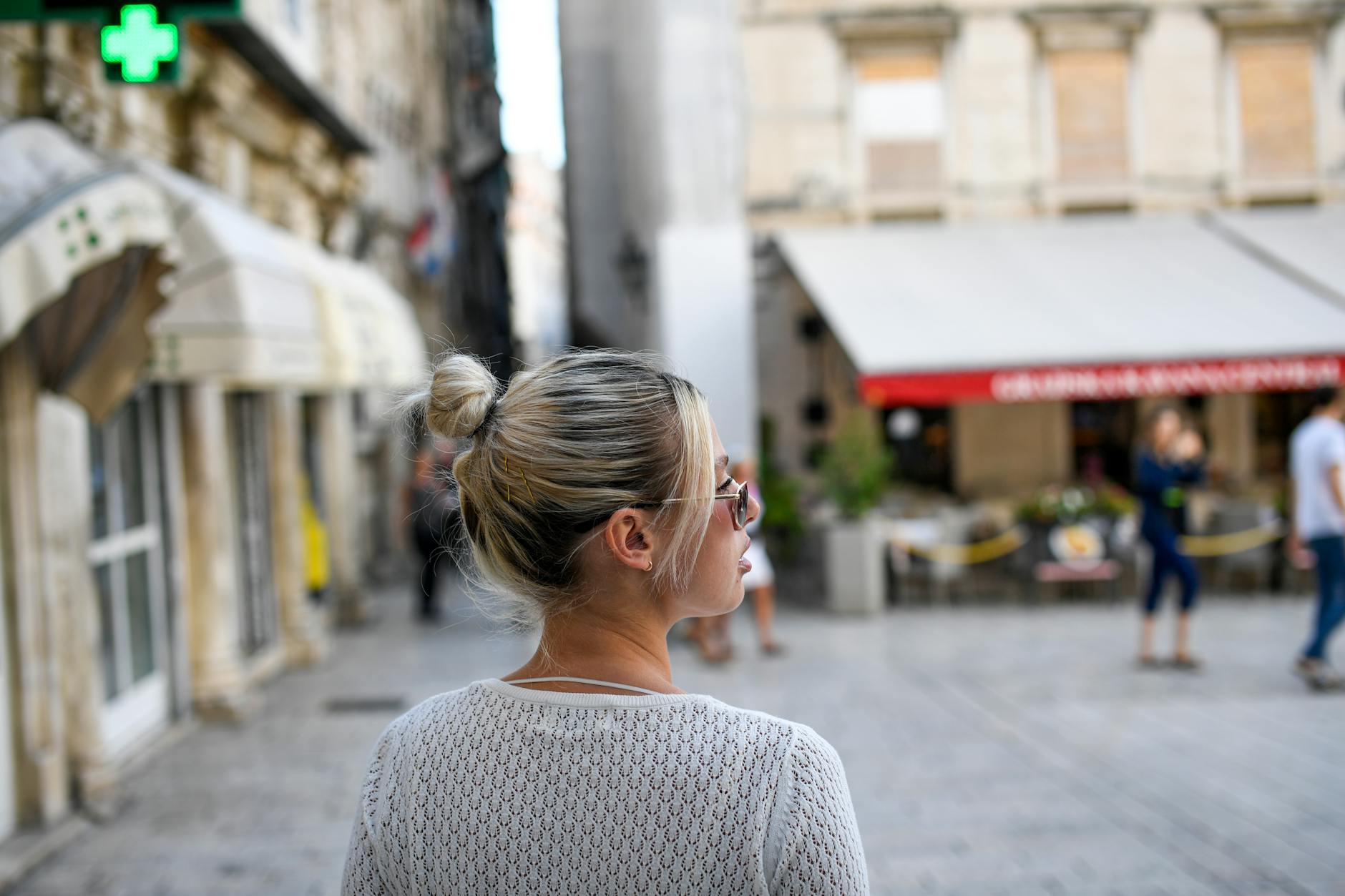 Outfit — A young woman with sunglasses and bun hairstyle exploring a bustling city street in Croatia during summer.