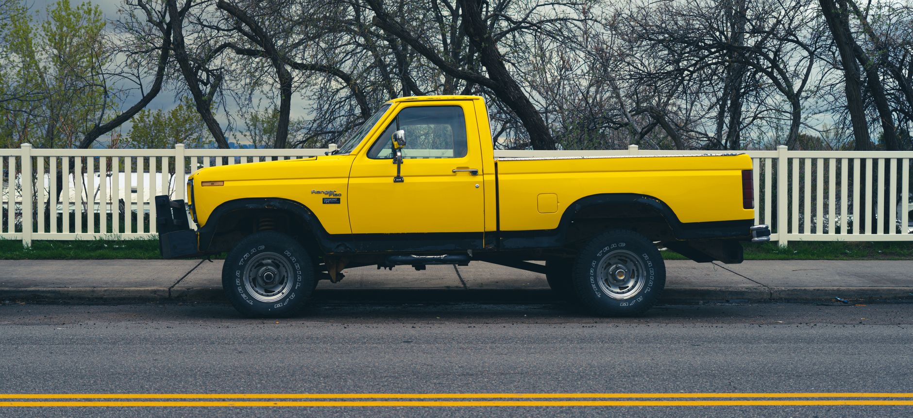 Pickup Line, Funny Pickup Lines, Smooth Pickup Lines, Pickup Line — Side view of a parked yellow pickup truck on a city street with trees