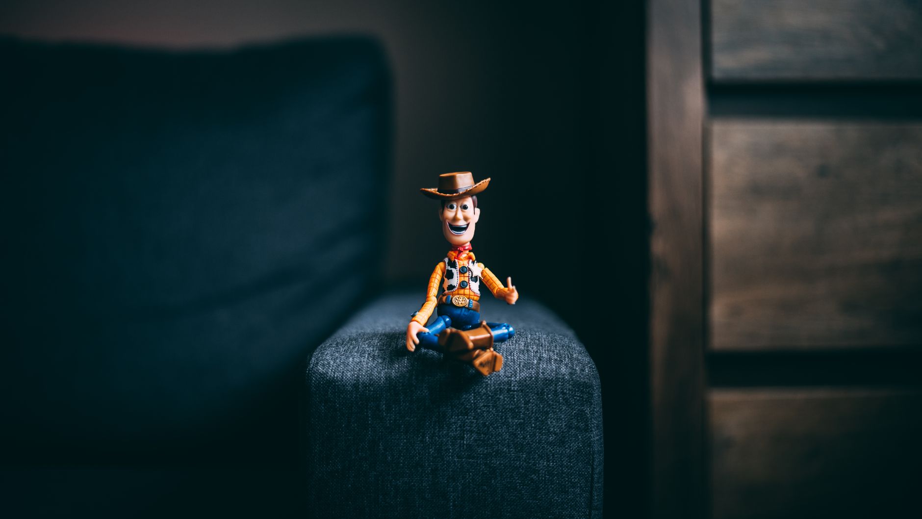 Pixar Character, Pixar Character, Pixar Style Character, 3d Character, Pixar — A toy cowboy figurine sits on the armrest of a gray sofa,