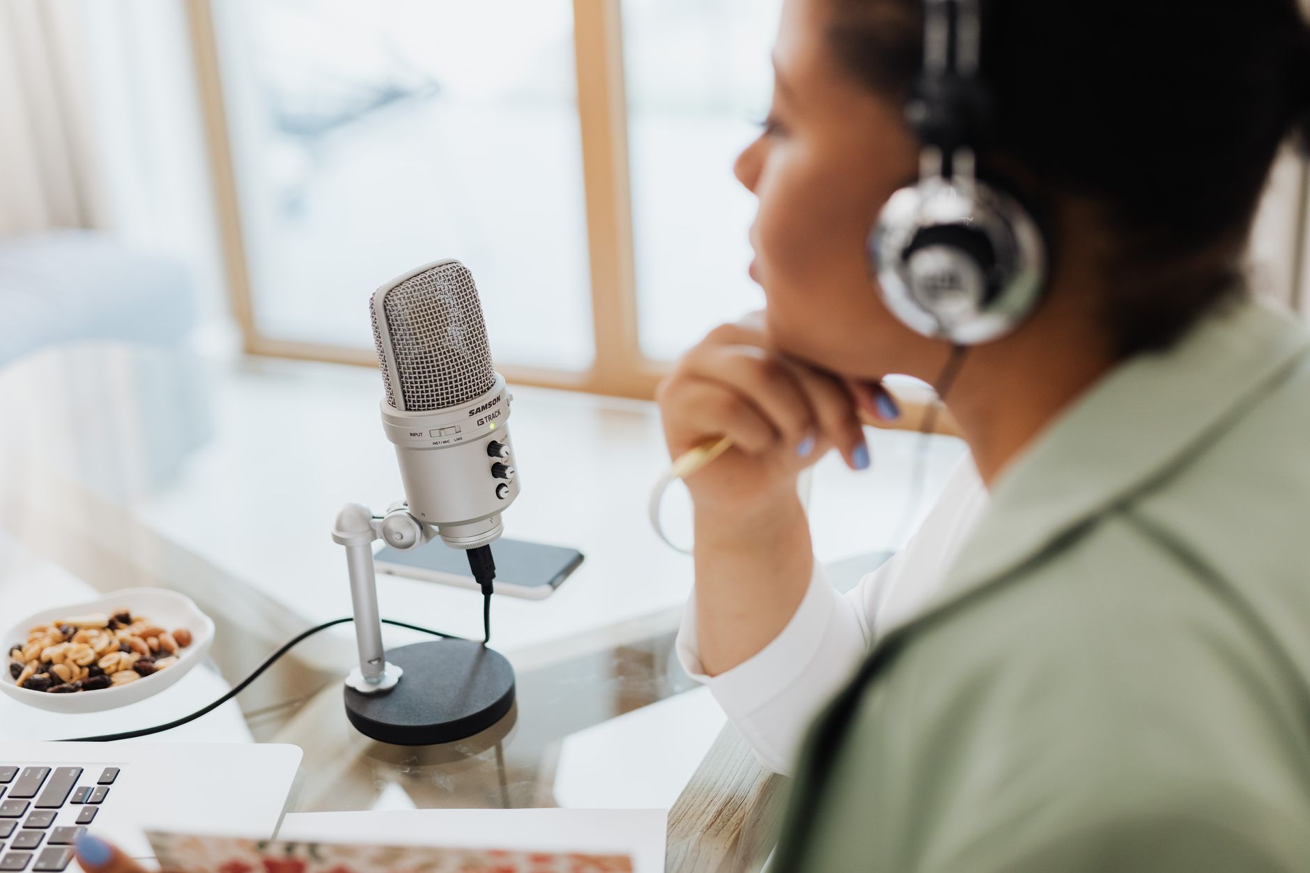 Podcast — Woman using laptop and microphone for podcasting at home.