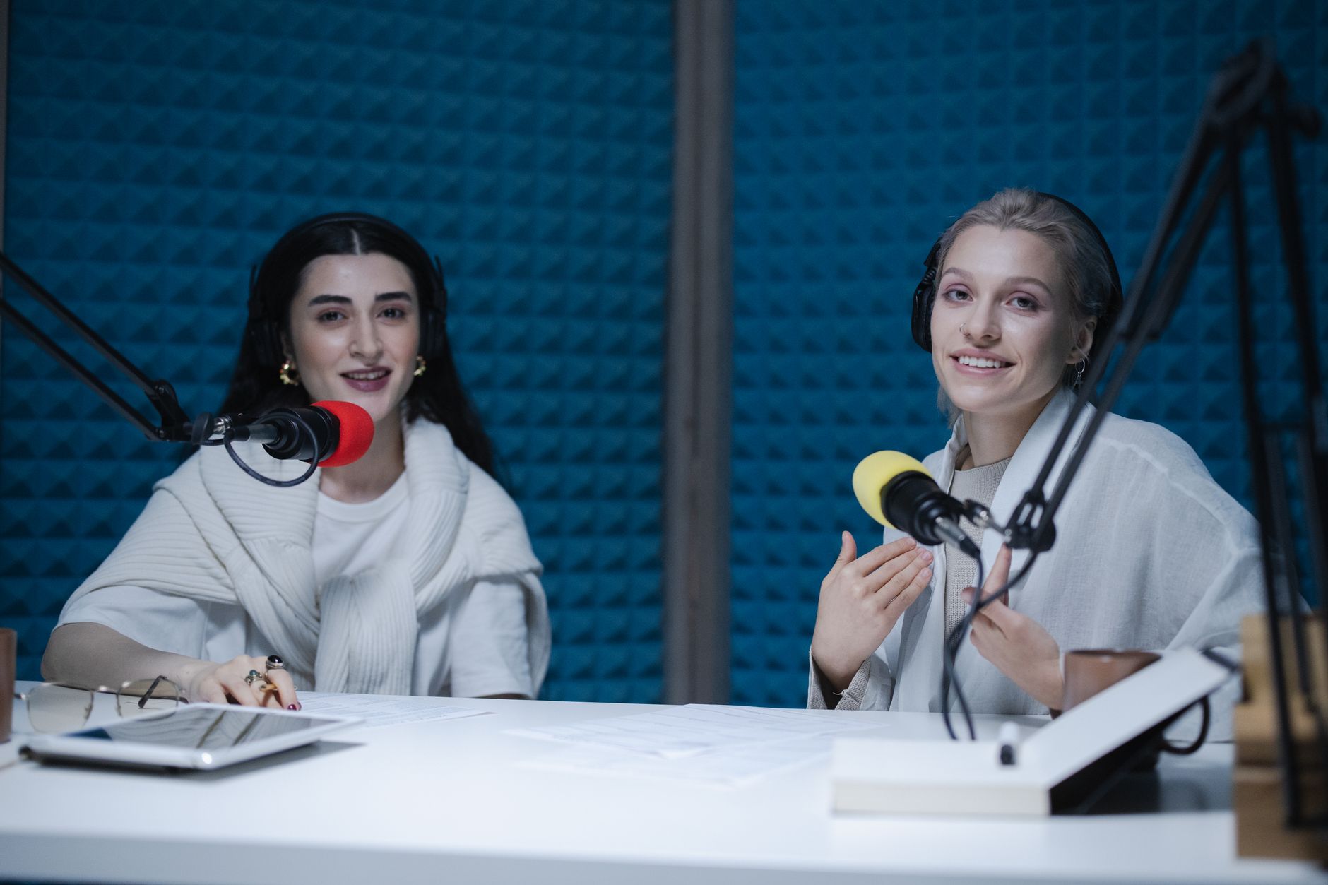 Podcast — Two women podcasters engaging in discussion inside a modern recording studio with microphones.