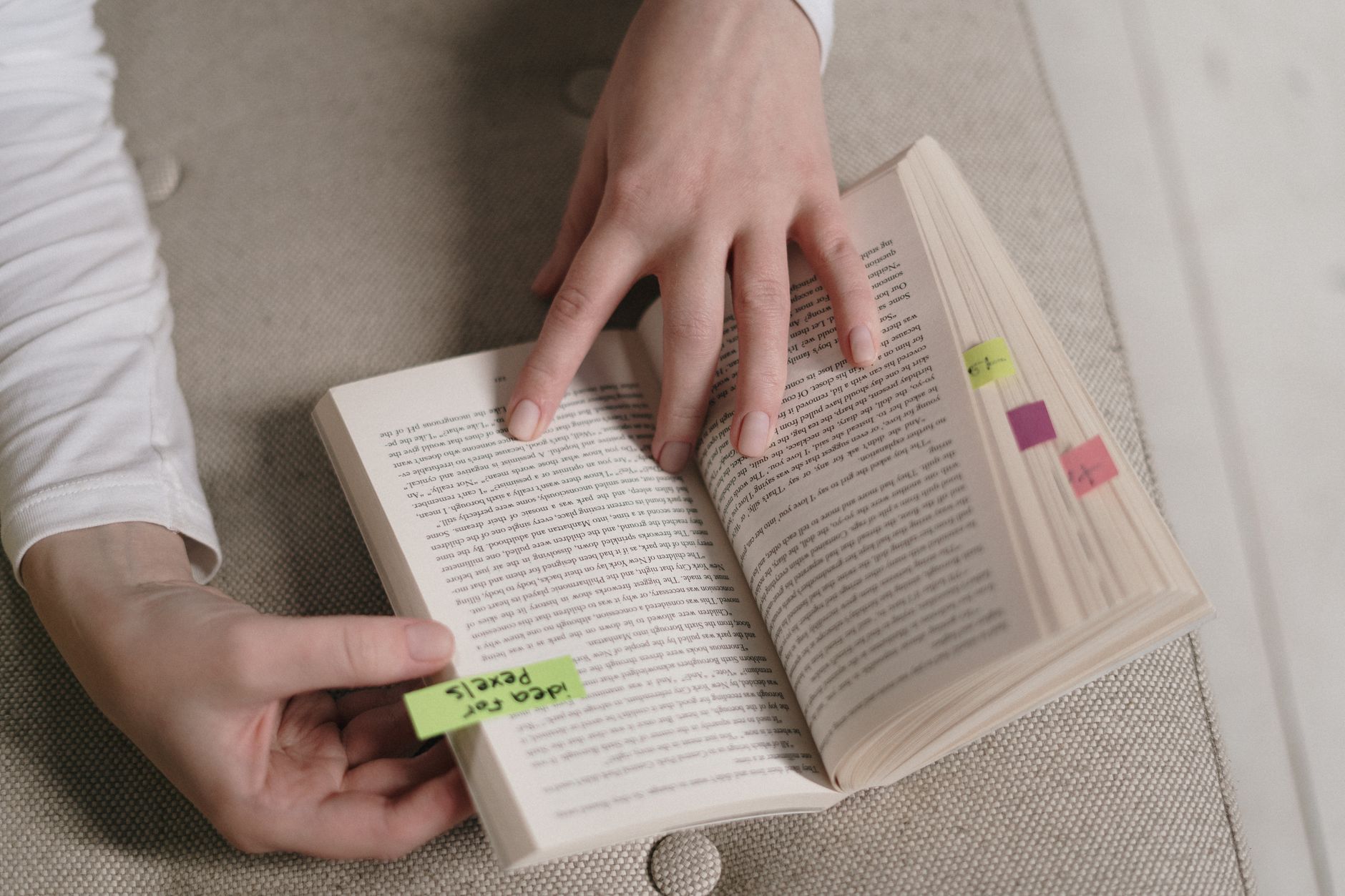 Prompts For Logo Design — An up-close view of hands holding an open book with colorful bookmarks, ideal for literary themes.