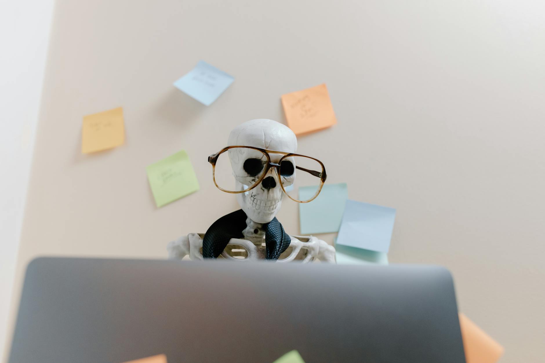 Skeleton Video — Skeleton wearing glasses uses laptop surrounded by sticky notes, symbolizing stress or burnout.