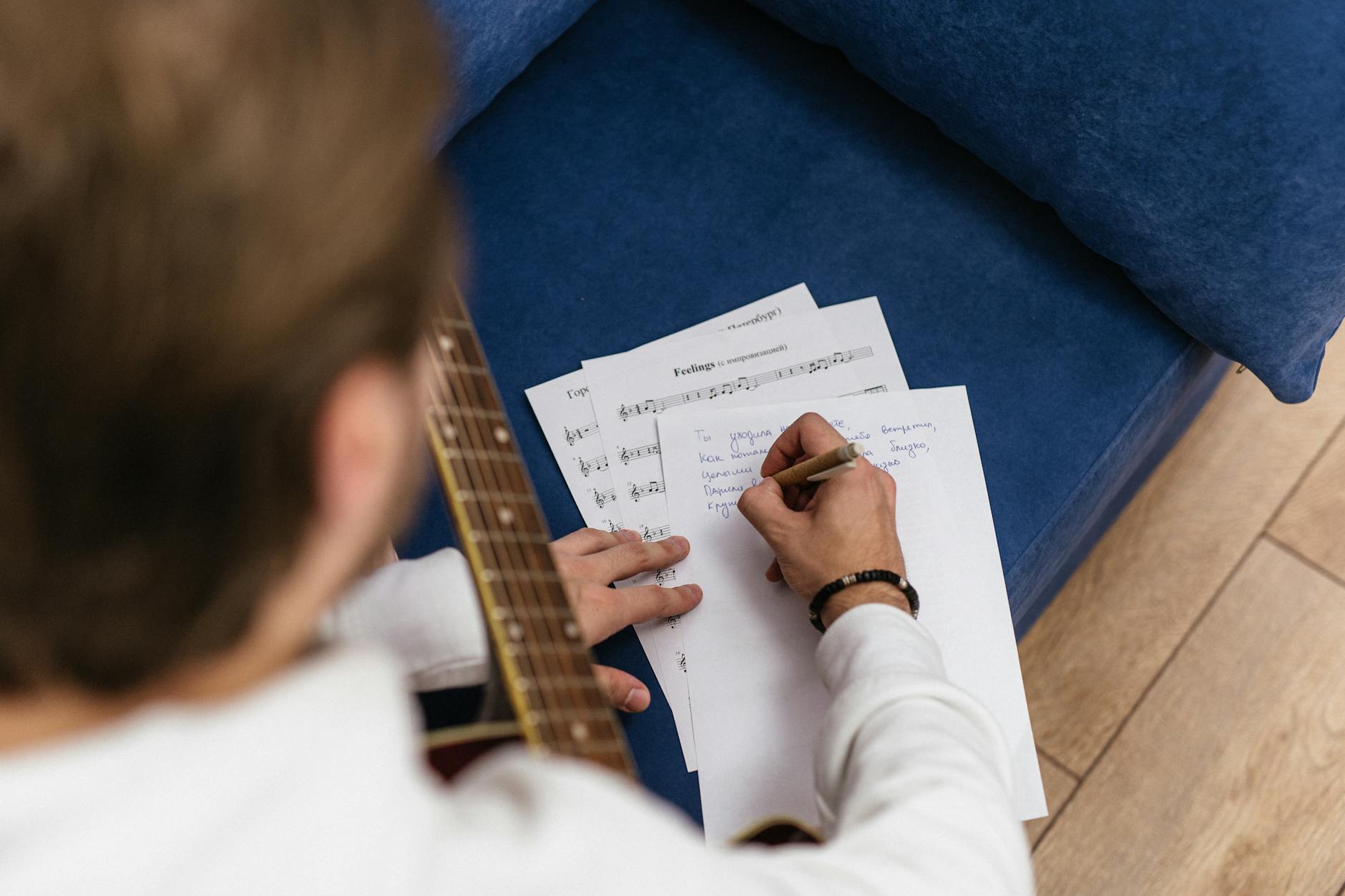 Song Lyrics, Lyric Writer, Song, Rap Lyrics — Man composing music on acoustic guitar with handwritten notes indoors.