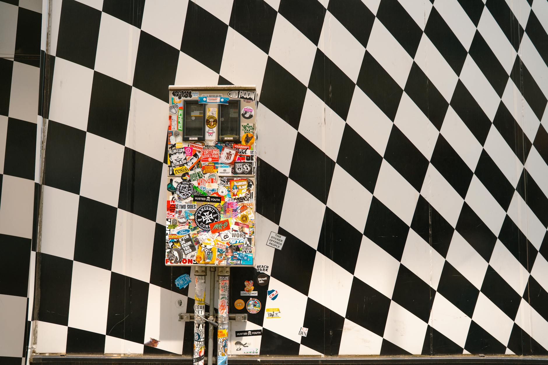 Sticker — A colorful sticker-covered utility box against a black and white checkered wall in Tokyo.