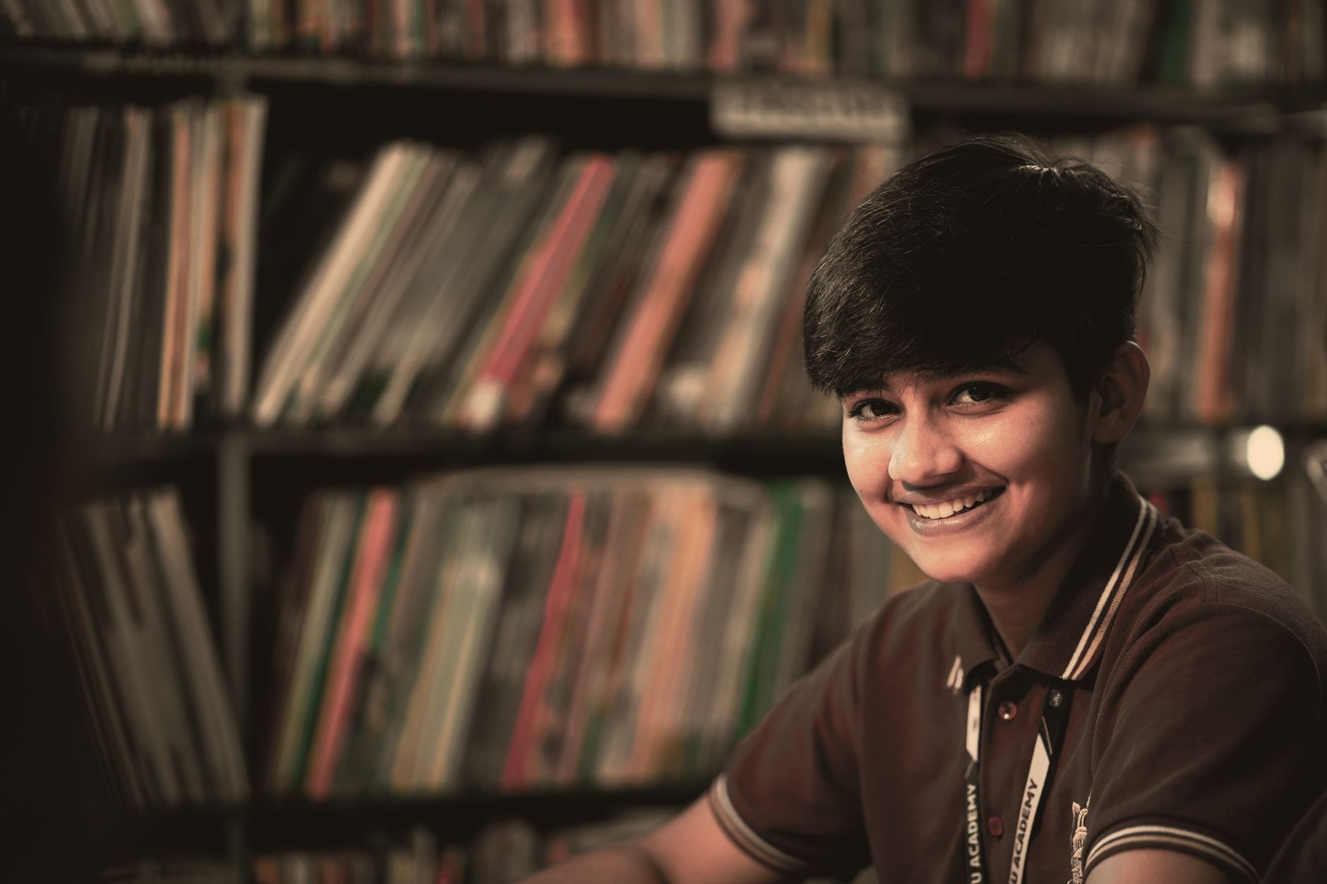 Best For Education — Joyful teenager smiling in a library, creating a warm academic atmosphere.