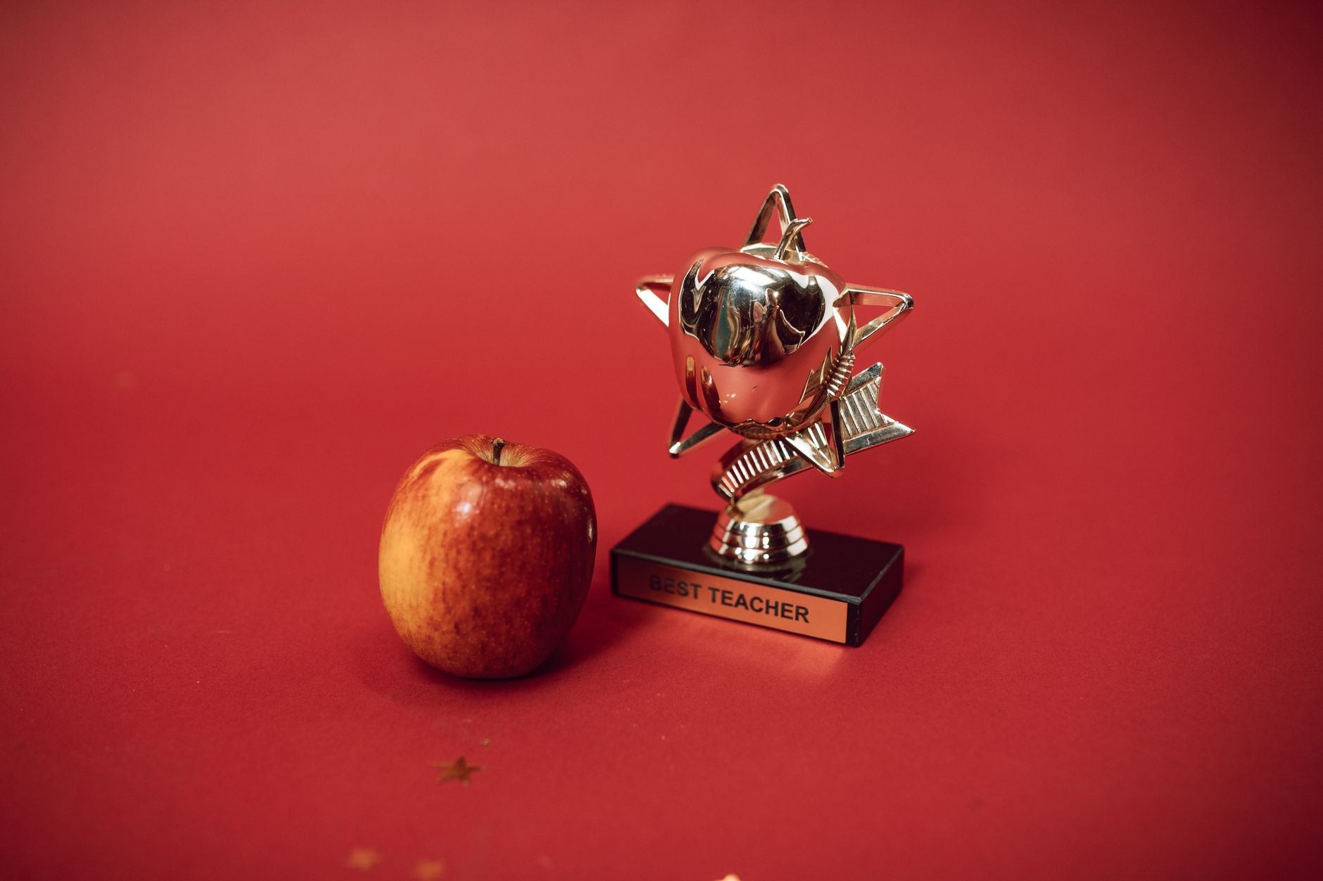 Best For Education — A Best Teacher trophy alongside an apple on a vivid red background symbolizing education and recognition.