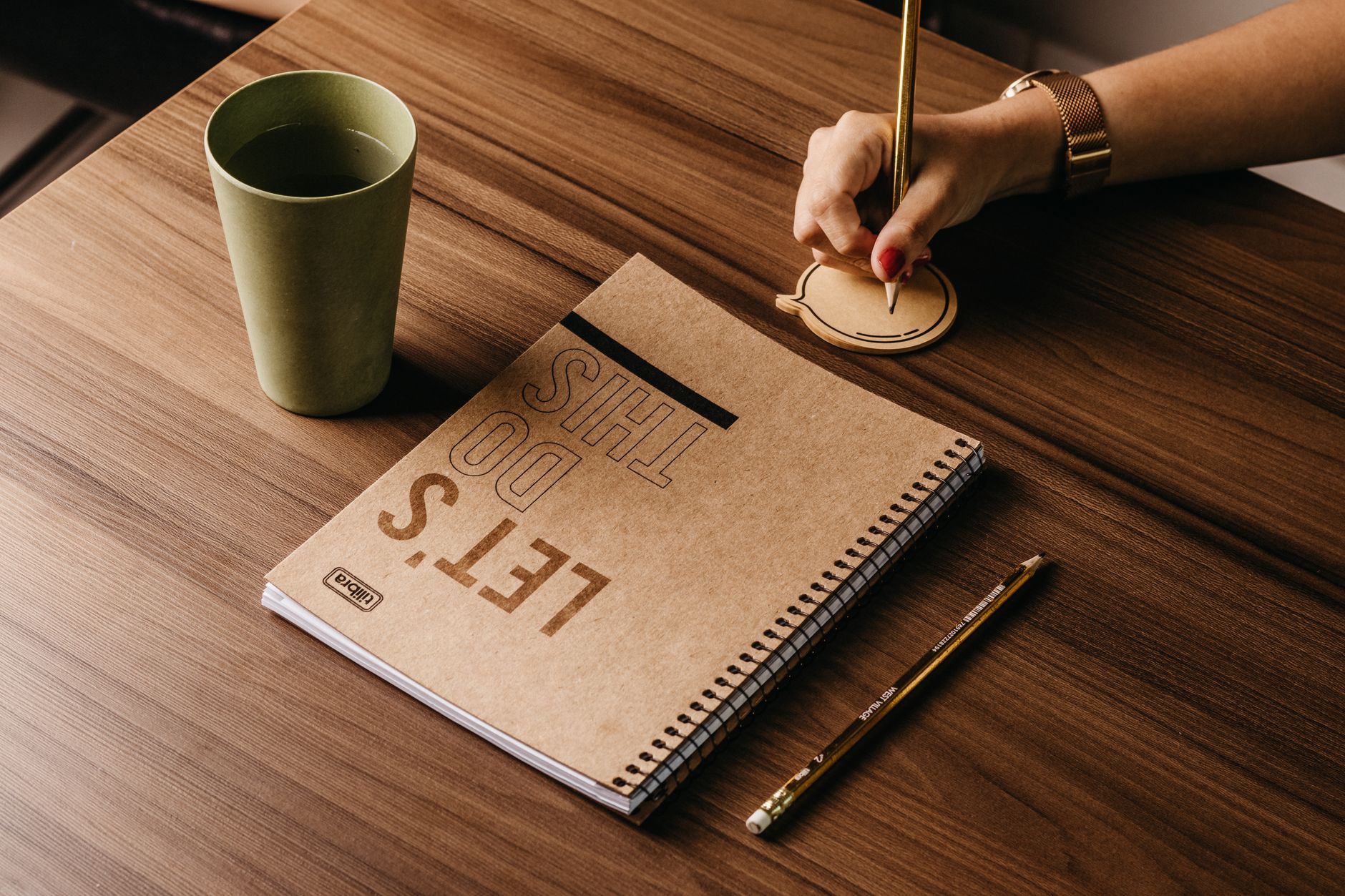 Best For Speech Writing — A woman s hand writing on a speech bubble notepad next to a cup and notebook on a wooden desk.