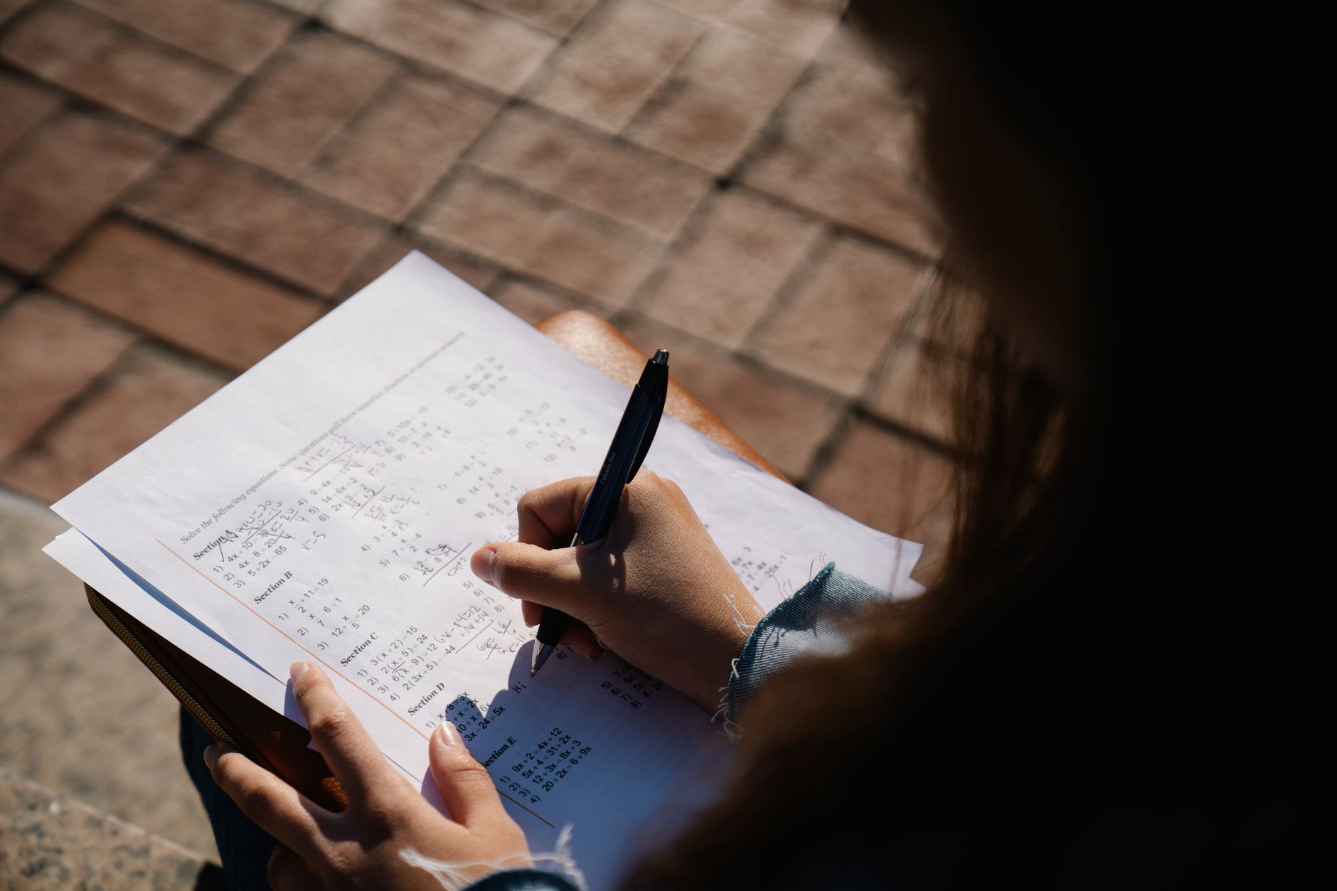 Study Guide — A person writing calculations on a mathematical worksheet with a pen outdoors.